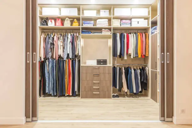 Photo of Modern wooden wardrobe with clothes hanging on rail in walk in closet