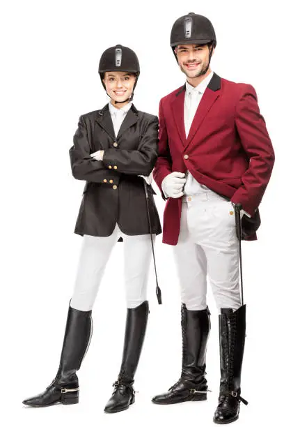 happy young equestrians in uniform and helmets looking at camera isolated on white