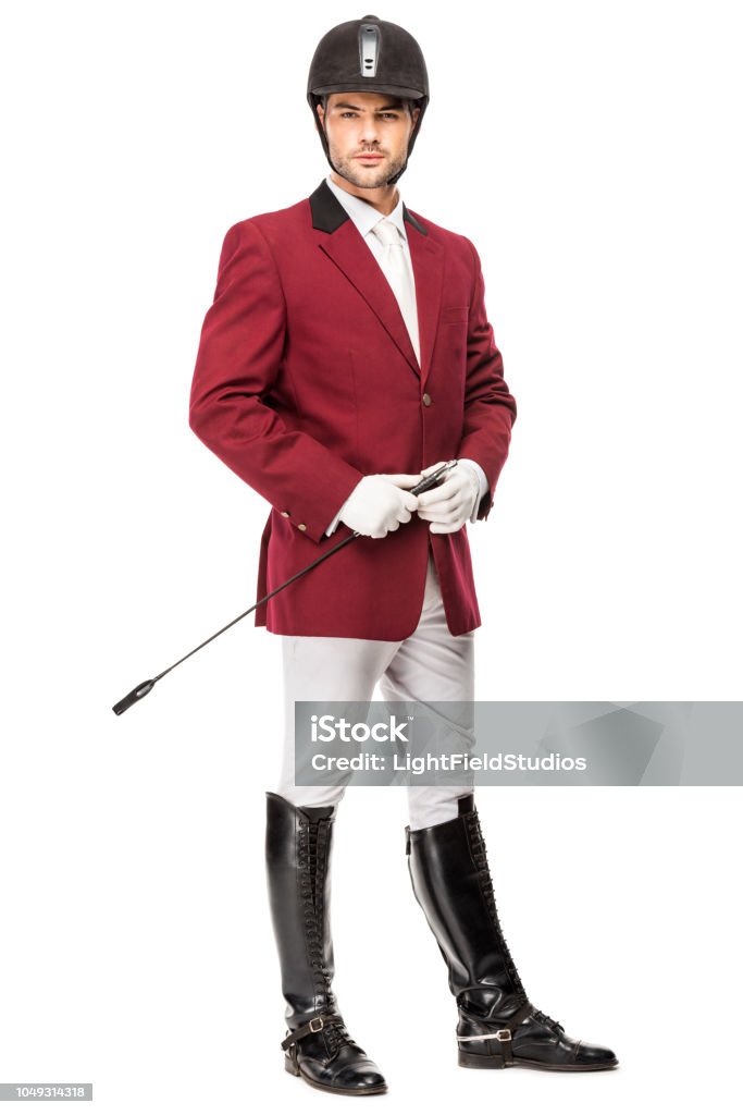 handsome young horseman in uniform holding horseman stick and looking at camera isolated on white Jockey Stock Photo