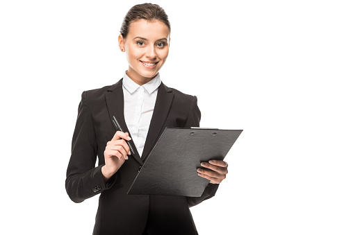 smiling young businesswoman in suit with clipboard looking at camera isolated on white