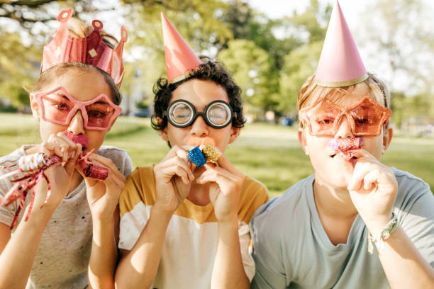 Funny smiling child clown on yellow background with multicolored balloons, copy space. April fools' day celebration concept. Birthday party concept
