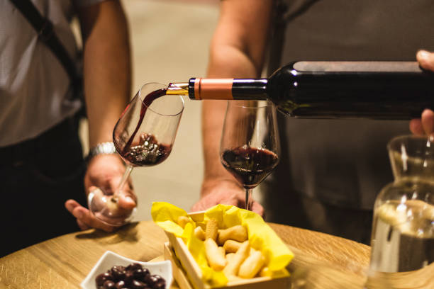 Close-up defocused people pouring wine behind the table with food (bread and olives) and glass of water.