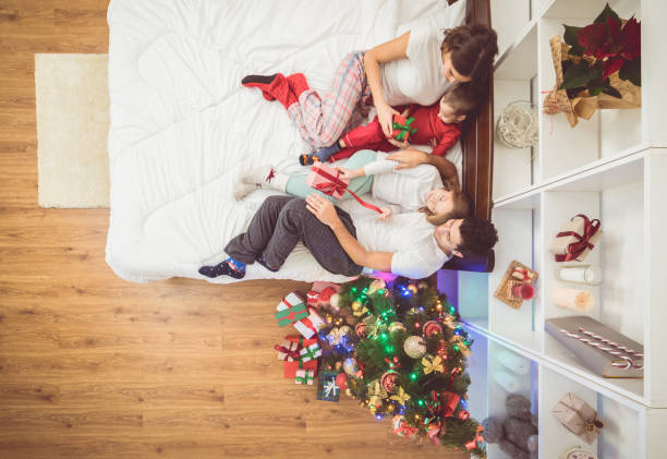 l’heureuse famille étends sur le lit près d’un arbre de noël. découvre d’en haut - placard holding celebration women photos et images de collection