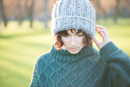 Backlit portrait of trendy young woman wearing warm winter woolies - wooly hat and knitted sweater. Great outdoors image with lots of copy space.