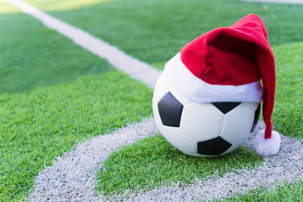 Santa Claus red hat on soccer ball at green grass stock photo