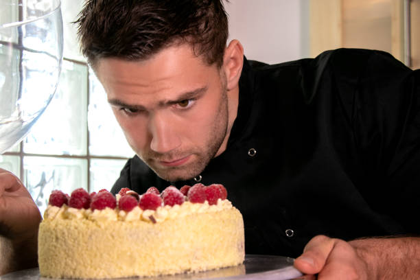 istock Good loooking baker busy icing cream cake and raspberries 1049335768