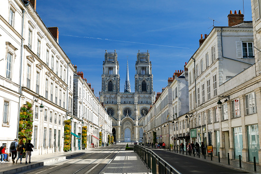 Orleans, France - September 29, 2018. Facade of the Cathedral of the Holy Cross (Cathédrale Sainte-Croix d'Orléans). Central perspective image - Joan of Arc Street (Avenue Jeanne d'Arc) with residential buildings left and right hand side. A few people in the streets.