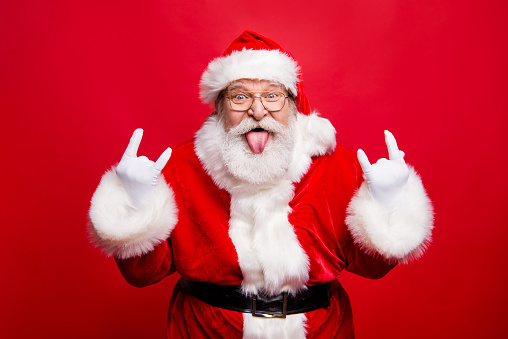 Ho-ho-ho! Party time concept. Aged mature playful emotion grandfather Santa with gloves sticking tongue out and comic grimace fooling around isolated on noel bright red background