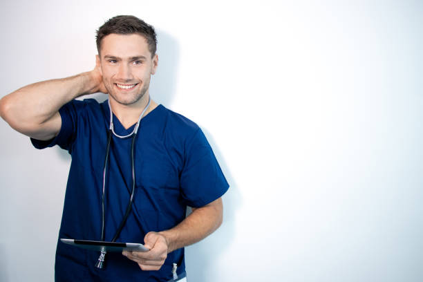 good looking male doctor or nurse in blue scrubs, holding digital tablet and laughing - healthcare and medicine nurse doctor general practitioner imagens e fotografias de stock