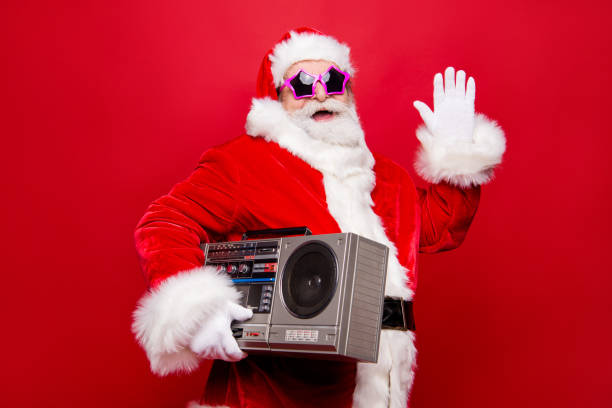 istock Profile side view aged funky white winter beard mature Santa modern star spectacles headwear costume hold audio record player make gesture hello goodbye isolated on December noel red background 1049349504
