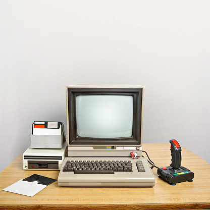 An old computer on a desk with a joystick and floppy disks. 
Blank screen to insert your own message. 
Large copyspace in the background.
