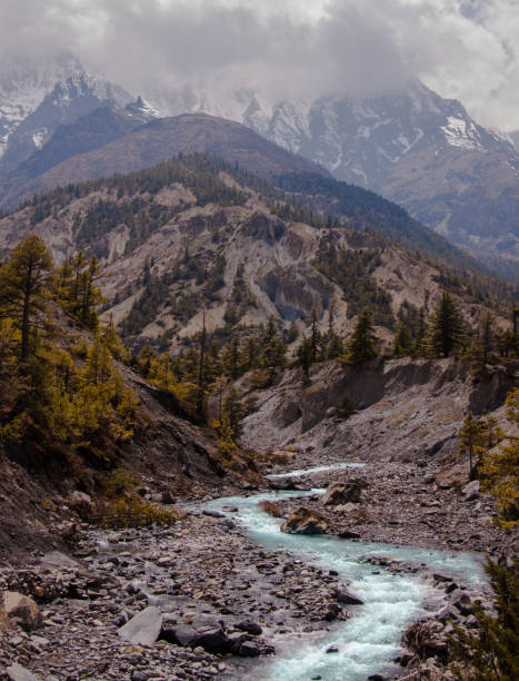 istock Scenic landscape with blue river, pine forest, cloudy peaks and snow mountain background. Annapurna circuit trekking route. Nepal. 1049350388