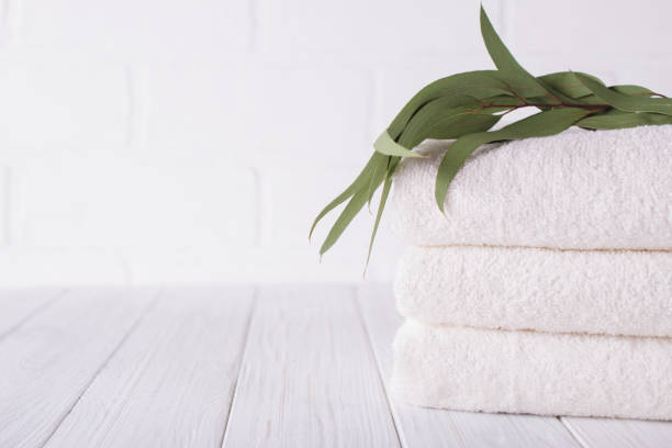 Spa composition on wooden table. Stack of three white fluffy bath towels with eucalyptus branch. Copy space