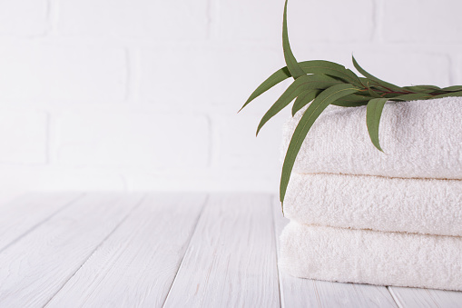Spa composition on wooden table. Stack of three white fluffy bath towels with eucalyptus branch. Copy space