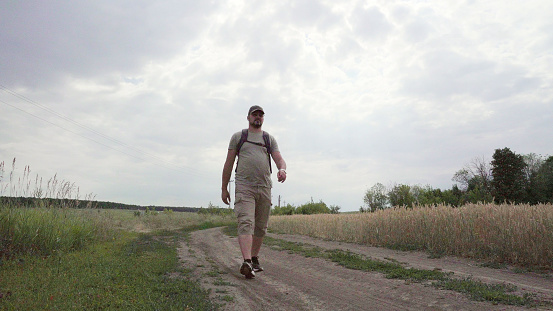 The traveler is on the road. Adult man. European type. Countryside. Ripe wheat fields. Summer time. Cloudy day.
