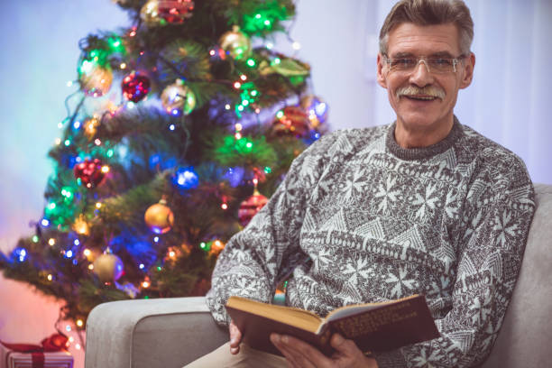 istock The smile old man with a book sit near the christmas tree 1049357364