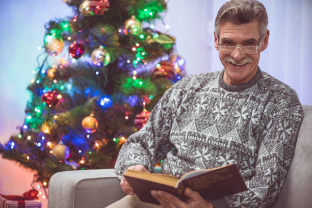 istock The smile old man with a book sit near the christmas tree 1049357384