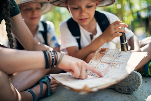Kids playing safari exploration trip. Brothers and sister sitting near wood cabin and reading an ancient treasure map. Note: ancient map is drawn by the author of the photo.\nSunny summer day.\nNikon D850
