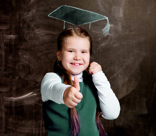 cute little schoolgirl against chalkboard, with drawn  cap stock photo