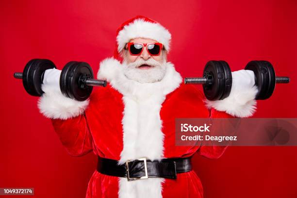 Portrait Of Nice Optimistic Positive Modern Stylish Strong Sporty Muscular Virile Saint Nicholas In Gloves Fur White Red Winter Clothes Holding Lifting Two Big Dumbbells Isolated Over Red Background Stock Photo - Download Image Now