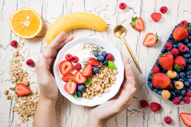 women's hands holding granola with berries, fruits, yoghurt and coffee for breakfast. cereal oats with strawberries, blueberries and raspberries for healthy eating. top view - eating women breakfast cereal imagens e fotografias de stock