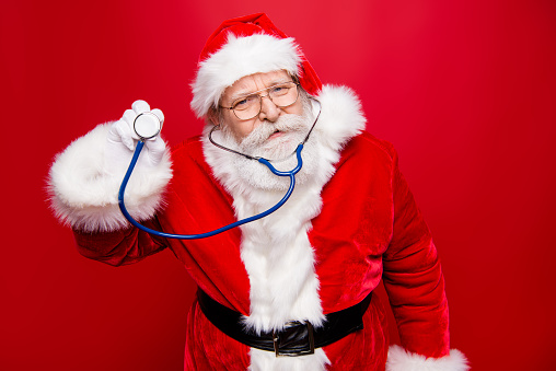 Worried calm Santa look at camera hold stethoscope in hand stand isolated on bright red background