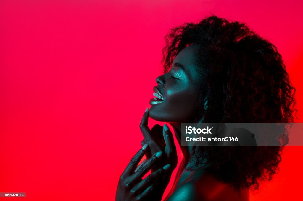 High Fashion model woman in colorful bright lights posing in studio High Fashion model woman in colorful bright lights posing in studio, portrait of african girl with trendy make-up. Art design, colorful make up. Over colourful vivid background. One Woman Only Stock Photo