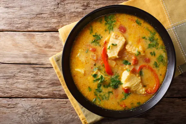 Brazilian food: Moqueca Baiana of fish and bell peppers in spicy coconut sauce close-up on a plate on a table. horizontal top view from above