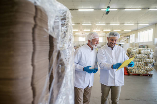 istock Two male managers in sterile clothes standing in warehouse and checking documents of package prepared for transport. 1049406644