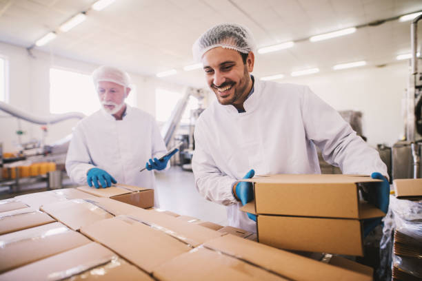 dos colegas masculinos me estéril ropa preparar cajas con productos para el transporte. en luminosa sala o almacén y conteo de paquete. - food hygiene fotografías e imágenes de stock