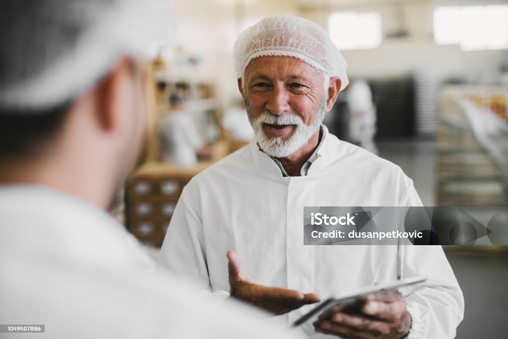 Photo de l’homme d’affaires de matures en vêtements stériles, discutant avec son collègue. Debout dans l’agro-alimentaire et parler affaires... - Photo de Usine agro-alimentaire libre de droits