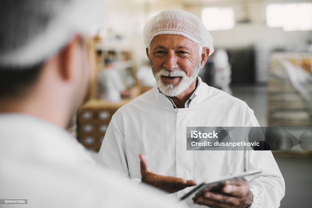 Picture of mature business man in sterile clothes talking with his colleague. Standing in food factory and talking about business.. Food Processing Plant Stock Photo