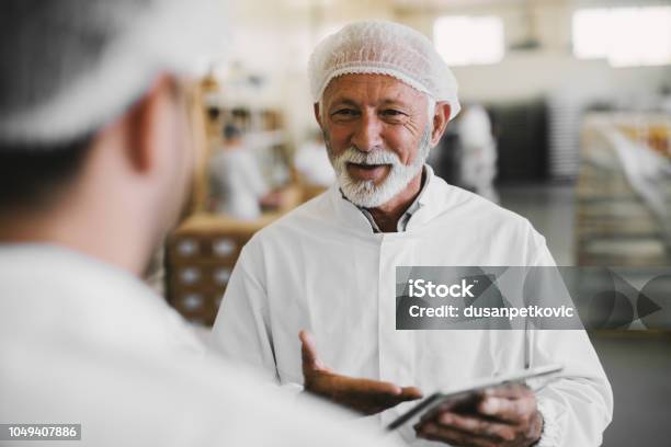 Picture Of Mature Business Man In Sterile Clothes Talking With His Colleague Standing In Food Factory And Talking About Business Stock Photo - Download Image Now