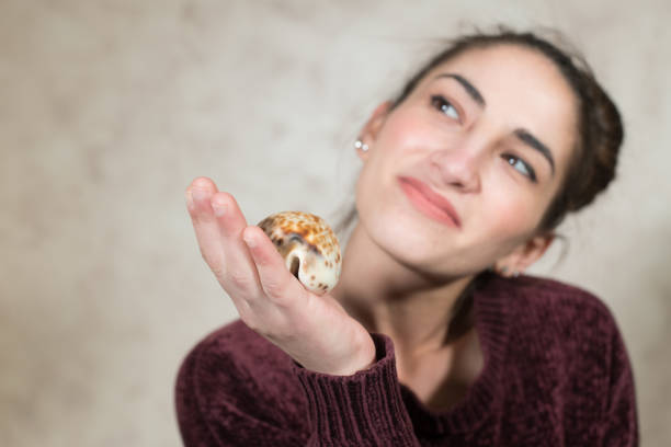 Human hands with sea shell offering and giving, woman smiling out of focus looking out, sea house concept