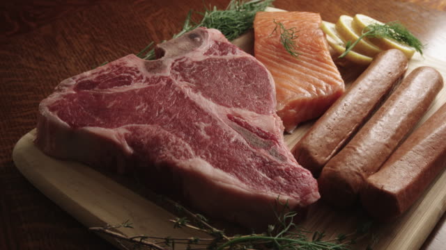 Raw T-Bone Beef Steak, Hot Dogs, and Salmon Gourmet Food on a Cutting Board