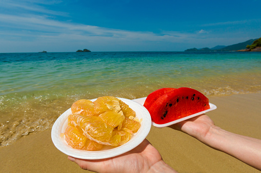 Two plates with watermelon and pomelo taken on beautiful thai seascape scenery. Fresh fruits on hands.