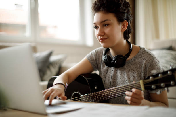 jeune fille souriante, jouer de la guitare à la maison - lyricist photos et images de collection