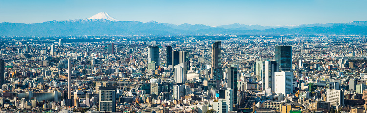 The iconic snow capped cone of Mt. Fuji overlooking the crowded cityscape and skyscrapers of downtown Tokyo.