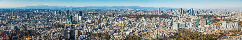 The iconic snow capped cone of Mt. Fuji overlooking the crowded cityscape and skyscrapers of downtown Tokyo.