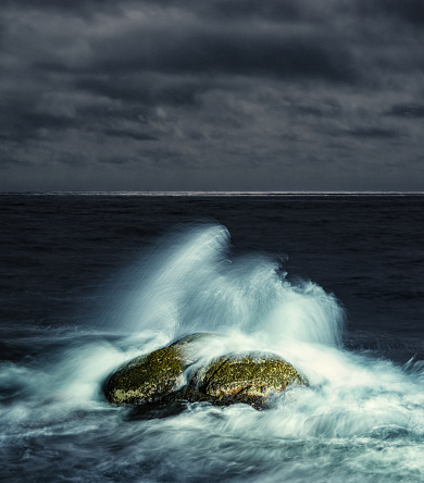 The spray of a crashing wave is illuminated at night.  Long exposure.