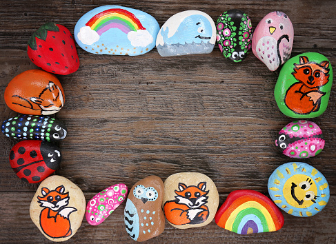 A colection of happy, colorful hand painted cartoon animal rocks are framing a wood plank background.