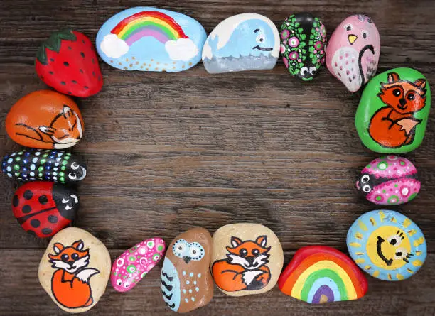 Photo of Border of Colorful Cartoon Hand Painted Animal Rocks on Wood Background