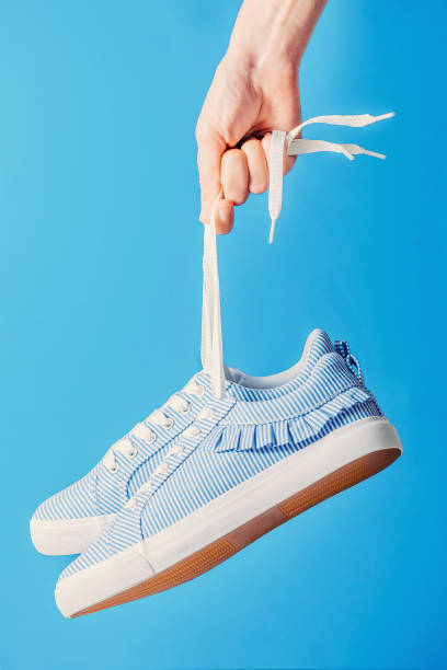istock hand holds hanging blue sneakers by the laces on blue background 1049472820