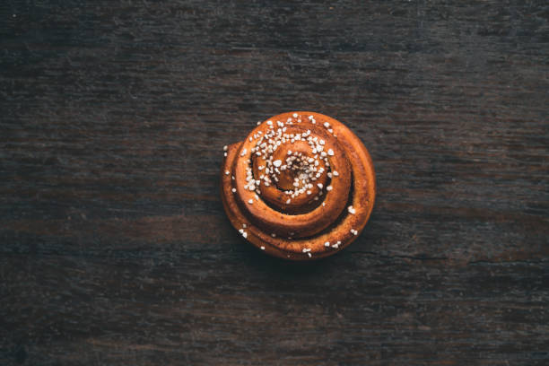 Traditional Swedish cinnamon bun on a wooden table Top down view of traditional Swedish cinnamon roll. Typical dessert in Sweden, especially for Cinnamon Bun Day. kanelbulle stock pictures, royalty-free photos & images