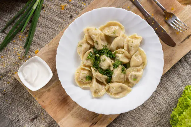 Russian National food. Top view of traditional belorussian meal. Dumplings in white plate with green and sour. Food concept.