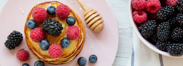 Pancakes with berries and honey on a pink plate, bowl of berries. Close-up. Top view.