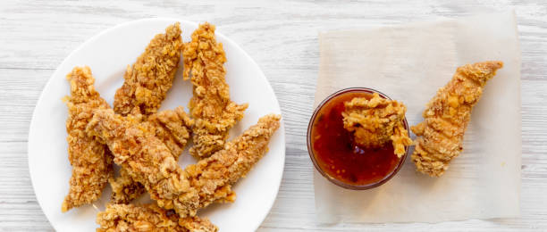 Spicy chicken strips on white plate with sauce over white wooden surface, overhead view. Flat lay, from above, top view. Close-up. Spicy chicken strips on white plate with sauce over white wooden surface, overhead view. Flat lay, from above, top view. Close-up. chicken finger stock pictures, royalty-free photos & images