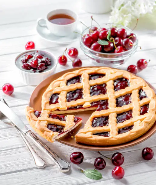 cherry tart on white wooden background served with fresh berries and cup of tea