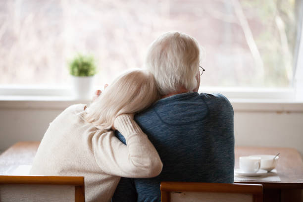 Rear view at senior grey haired couple relaxing at home Rear view at senior grey haired loving caring family couple embracing relaxing at home together enjoying peaceful morning breakfast looking at window view thinking of future feeling calm nostalgic sleeping grandpa stock pictures, royalty-free photos & images