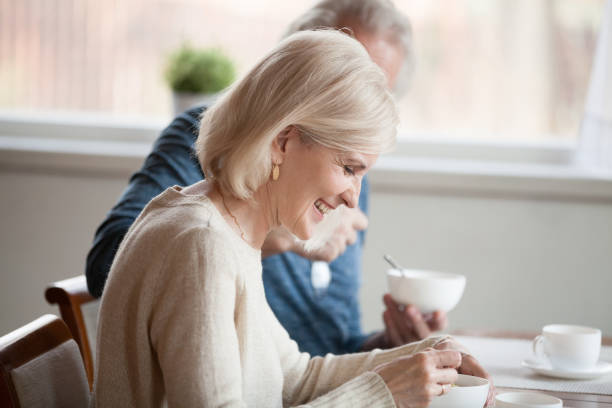 happy senior woman having breakfast with aged husband at home - aging process middle women men imagens e fotografias de stock